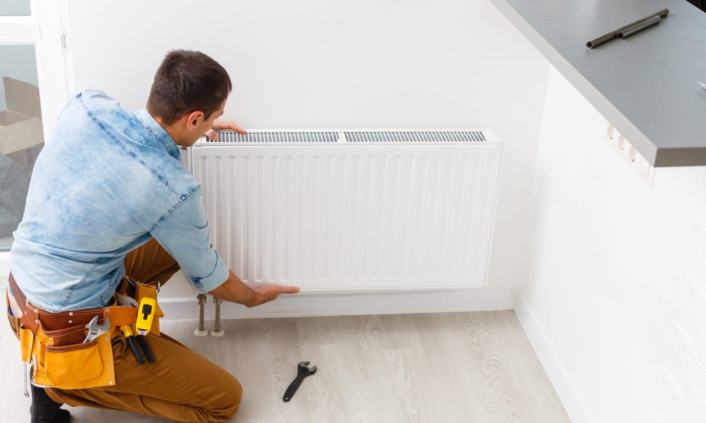 Man is repairing radiator battery in the room. Maintenance repair works renovation in the flat. Heating restoration. Wrench in hands.